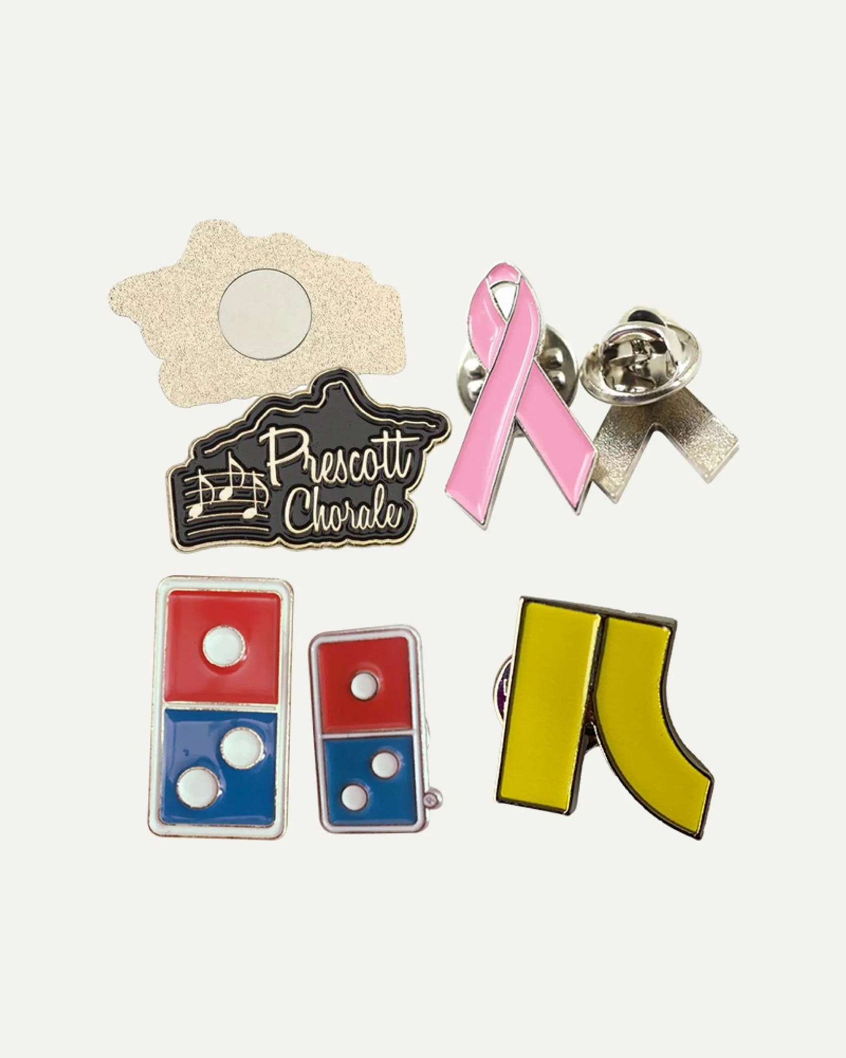 Collection of lapel pins including a pink ribbon, a 'Prescott Choral' badge, a yellow shoe, a 'domino' badge, and a flame-shaped badge with a circle cutout.