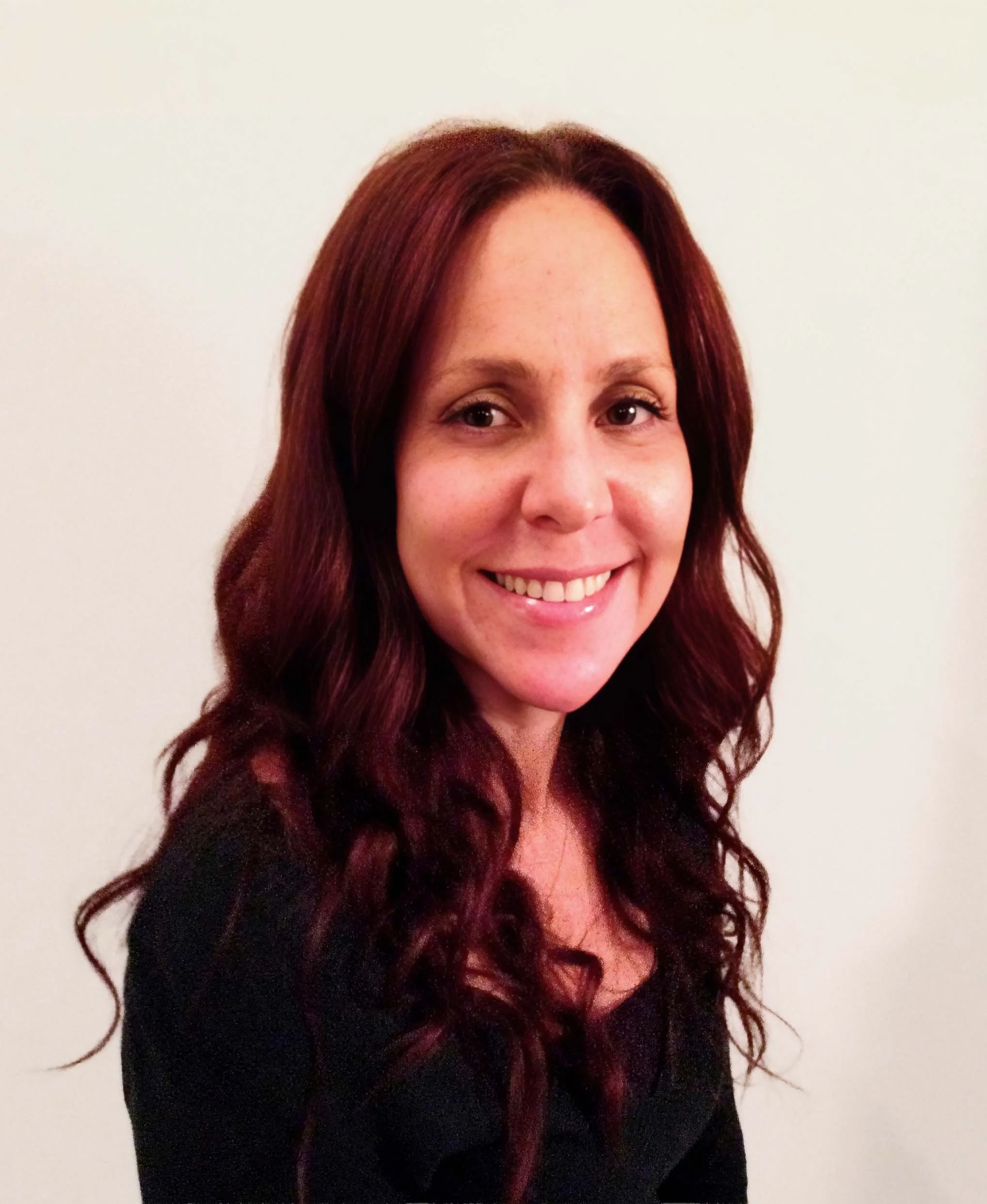 A woman with long, wavy, dark red hair smiling at the camera against a plain white background.