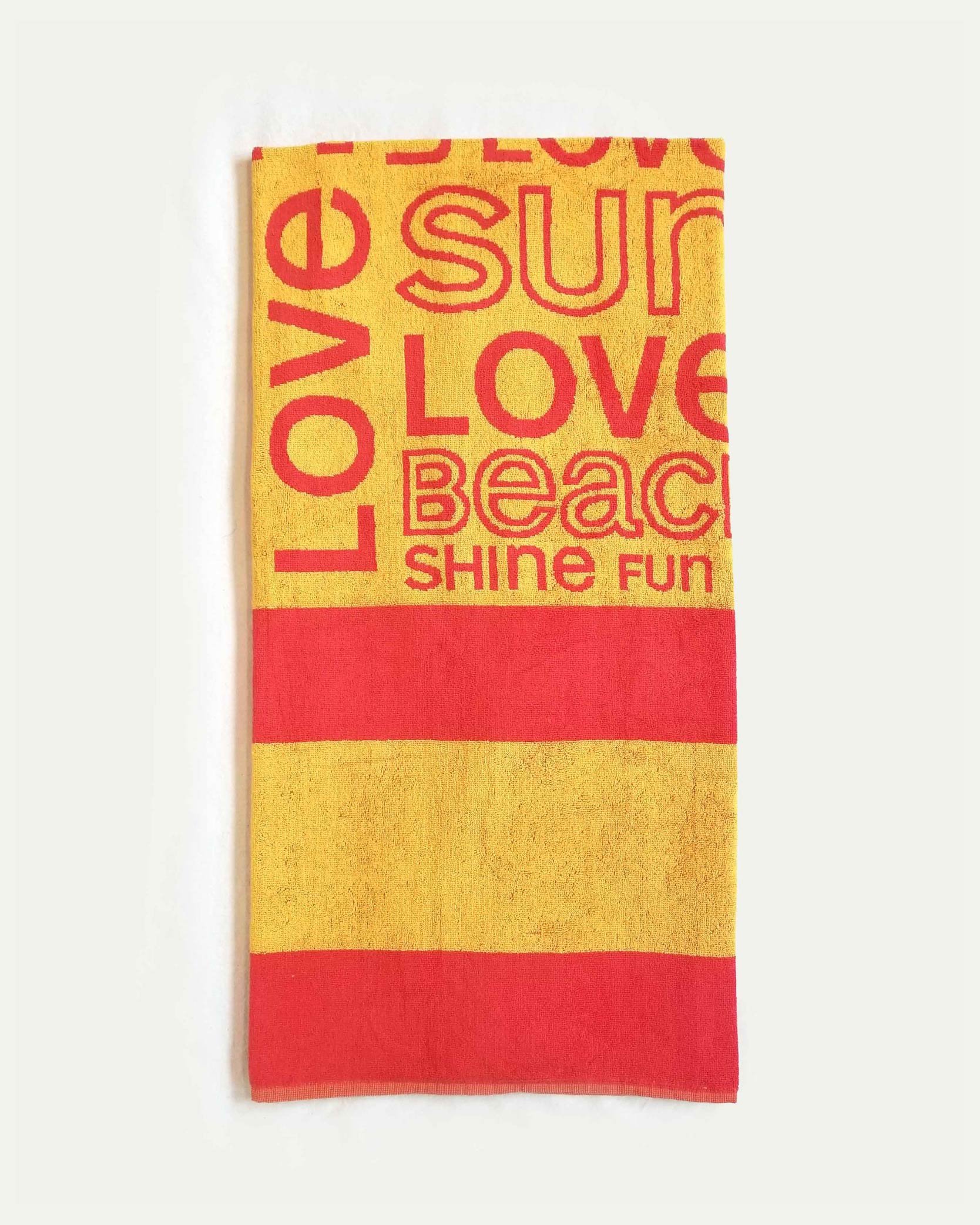 Colorful beach towel with red and yellow stripes and words like "love," "sun," "beach," "shine," "fun" printed on it.