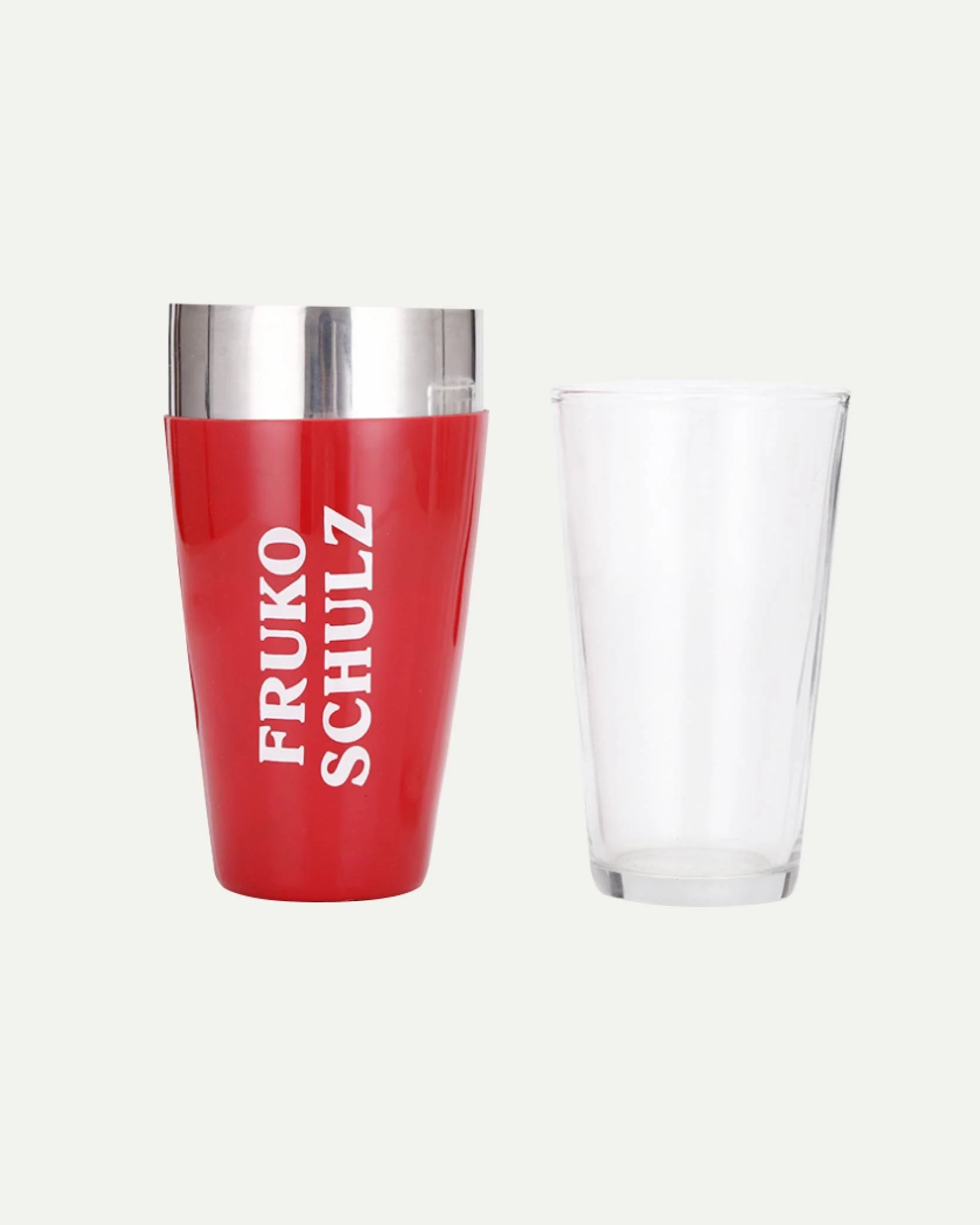 A red travel mug with "FRUKO SCHULZ" printed on it and a clear empty glass beside it on a plain background.