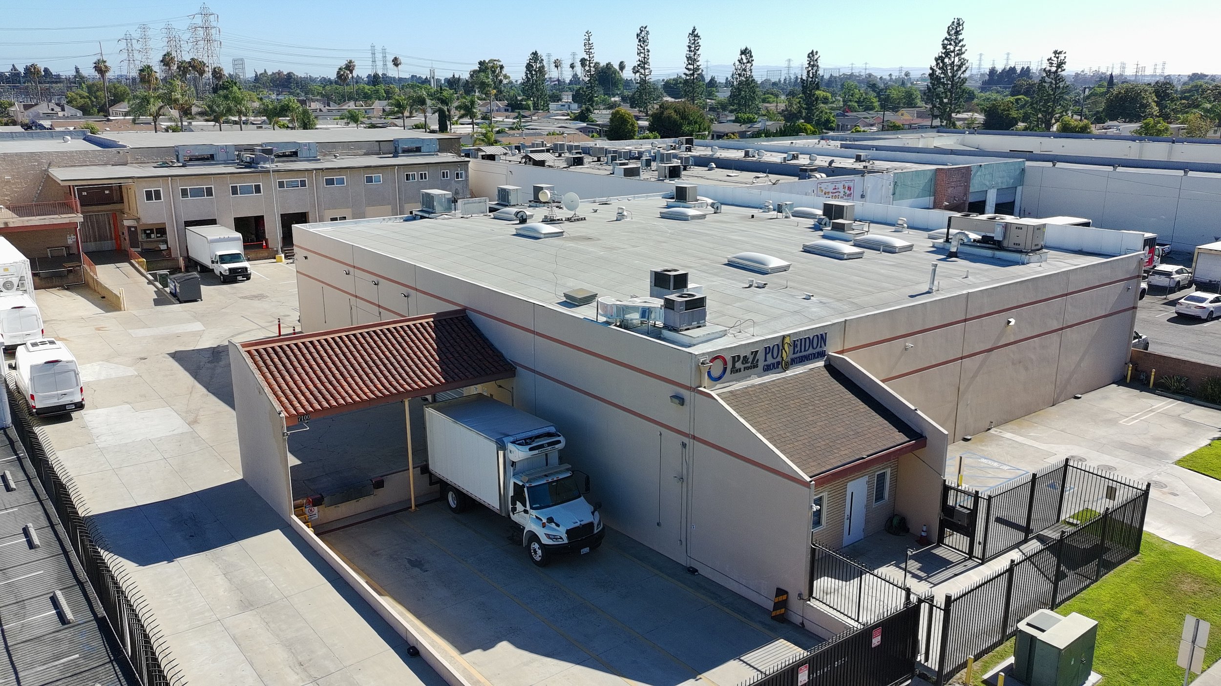Photo of a commercial warehouse with a parking lot and delivery trucks parked outside. The building has air conditioning units on the roof and a sign reading "P&Z POLE DION."