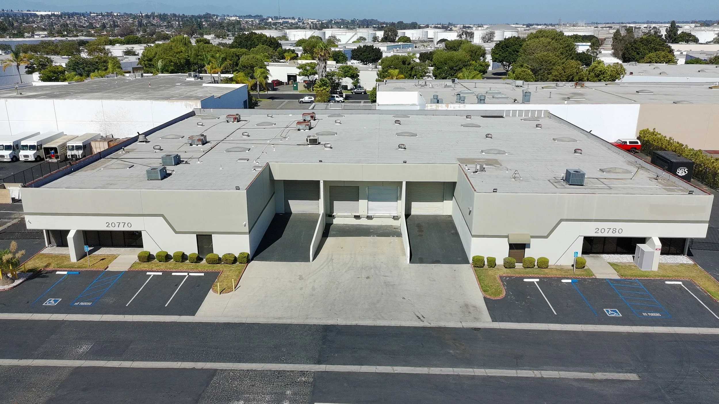 Aerial view of a commercial building with parking lot, surrounded by trees and distant buildings.