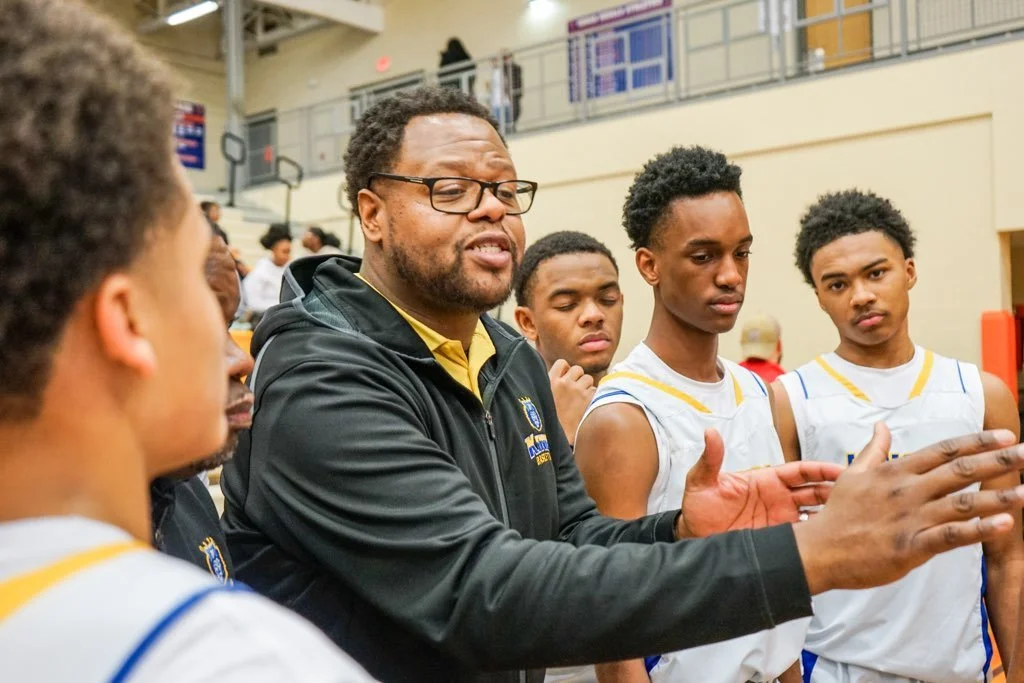 Basketball coach giving instructions to a young basketball team during a game or practice in a gymnasium.