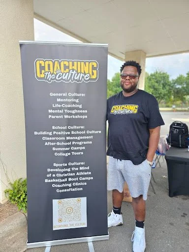 A man standing next to a banner that reads 'Coaching the Culture,' promoting programs on general, school, and sports cultures.