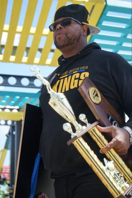 Man wearing sunglasses and a black Cap, holding a trophy during a celebration or award ceremony.