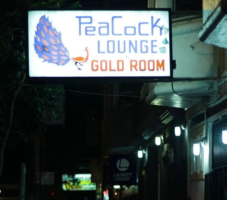 Illuminated sign for Peacock Lounge and Gold Room with a peacock feather and a peacock illustration