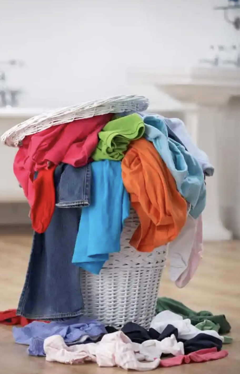 A laundry basket overflowing with colorful clothes, with some garments spilled on the floor.