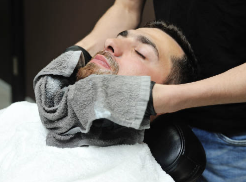 Man receiving a face massage in a spa or salon, lying on a treatment table with a towel around his neck and a cloth covering his eyes.
