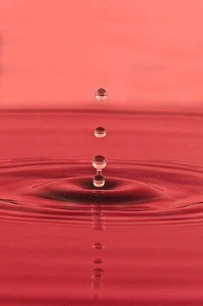 Three water droplets falling into a pink-colored water surface, creating ripples.