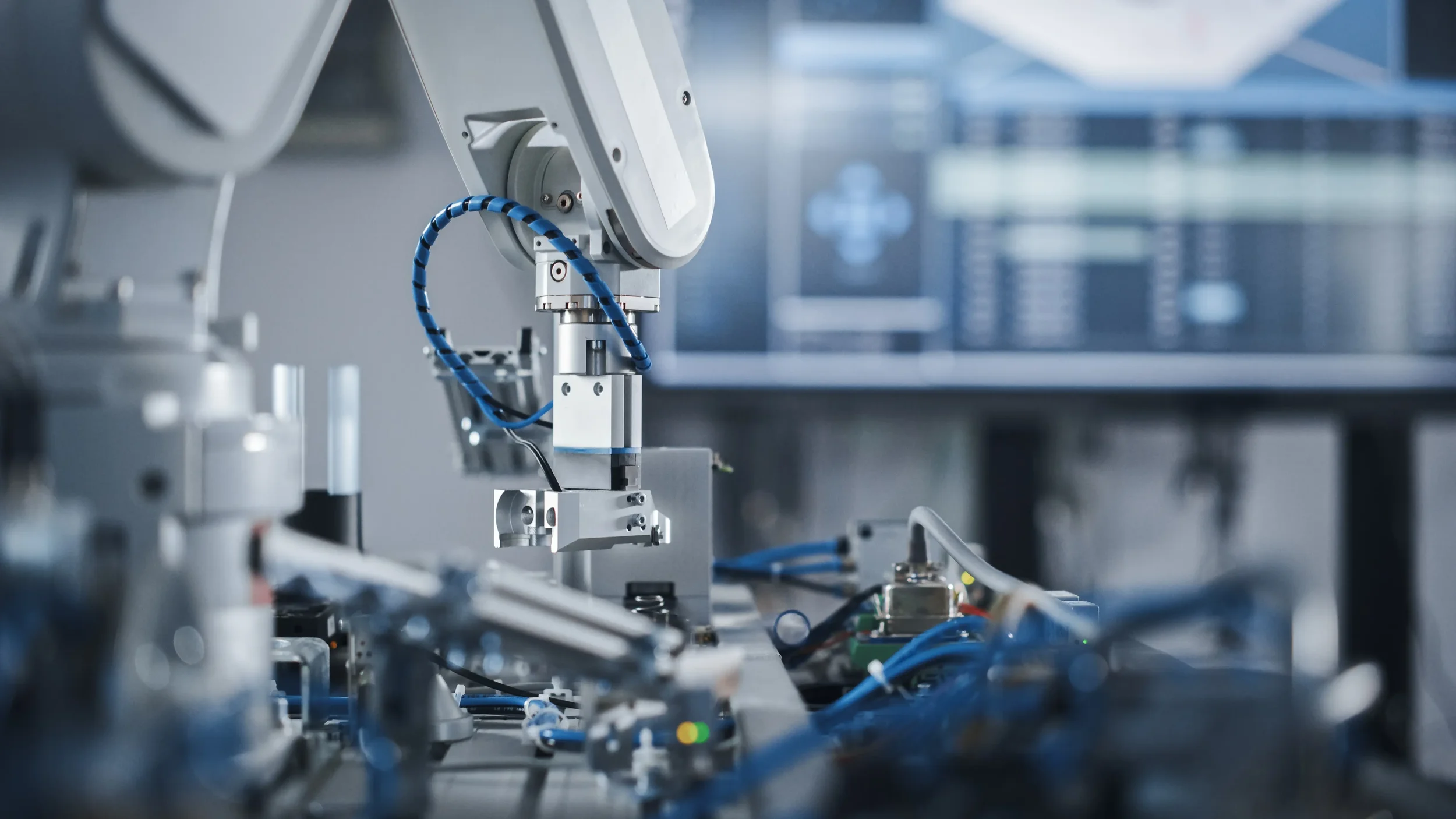 Close-up view of industrial robotic equipment with metal components, wires, and blue cables in a high-tech manufacturing facility.