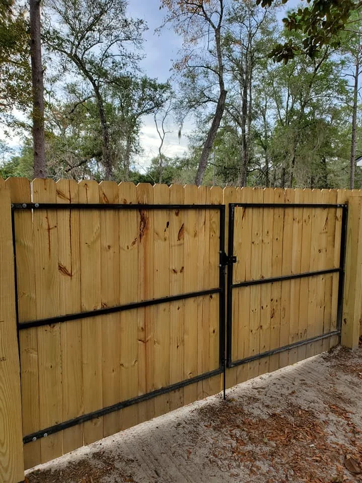 New wooden privacy fence with a black metal gate in a backyard.