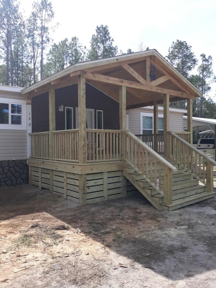 A newly built wooden porch with stairs and railing attached to a house.
