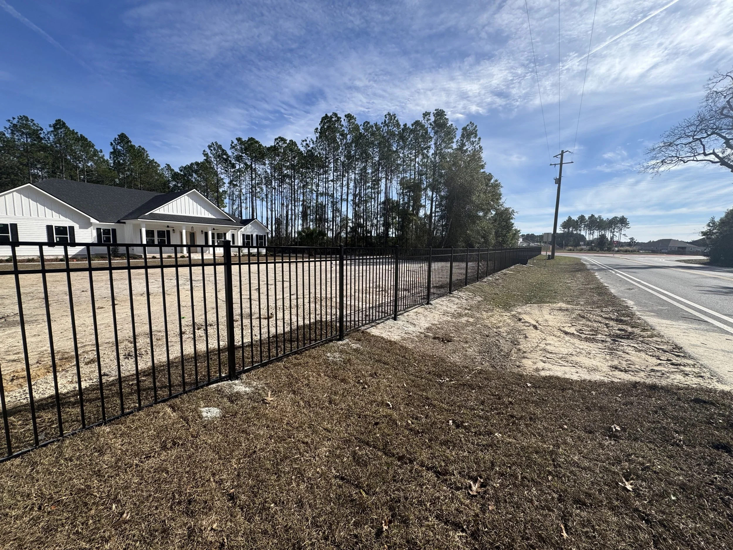 A newly constructed house with black shutters and a black roof, behind a black metal fence, on a partly cloudy day.