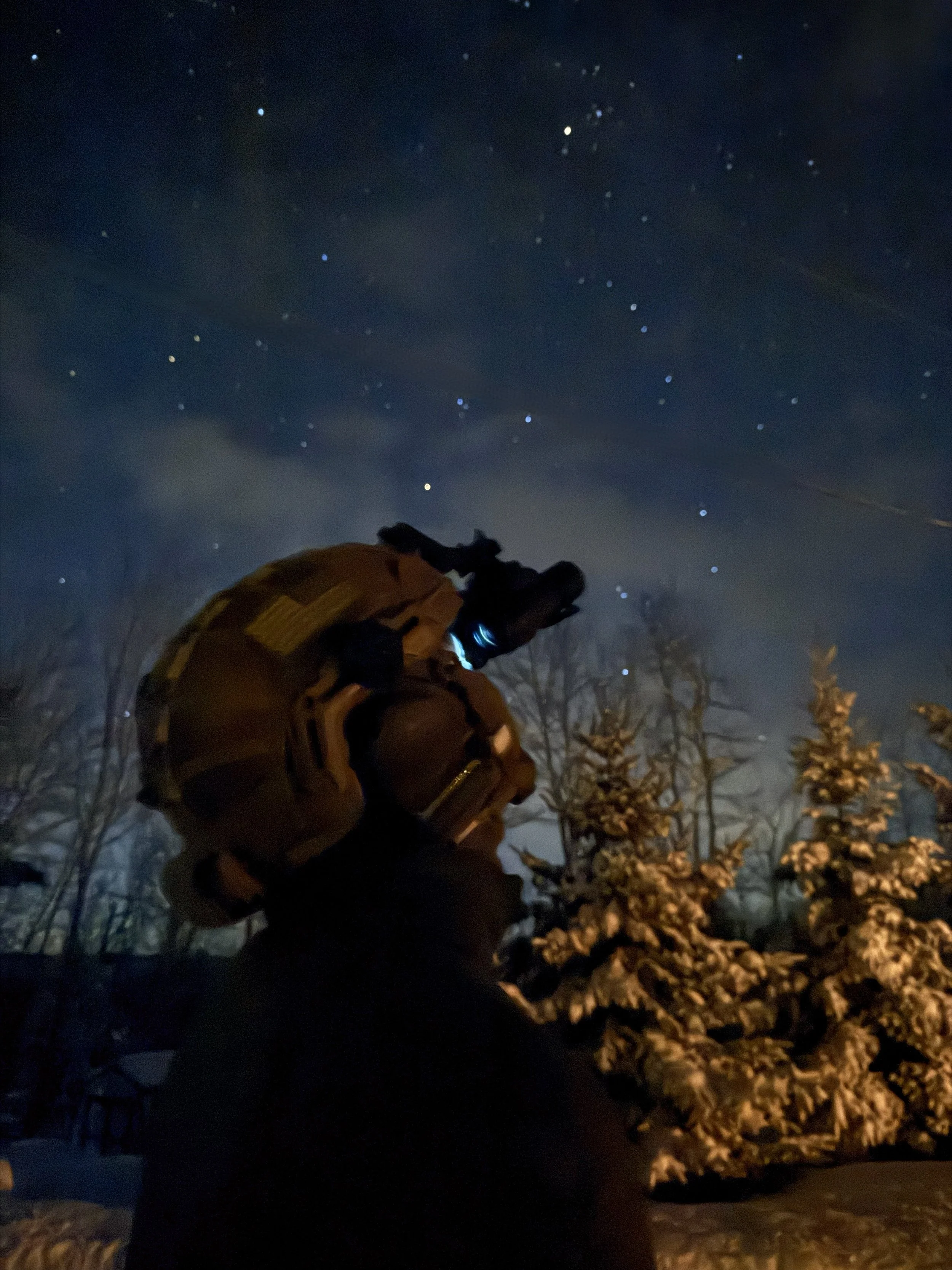 Tactical, NODs, NVG, NVGs, BNVD, camouflage gear and a  high cut helmet looking through BNVDs at night, with a starry sky and snow-covered trees in the background.