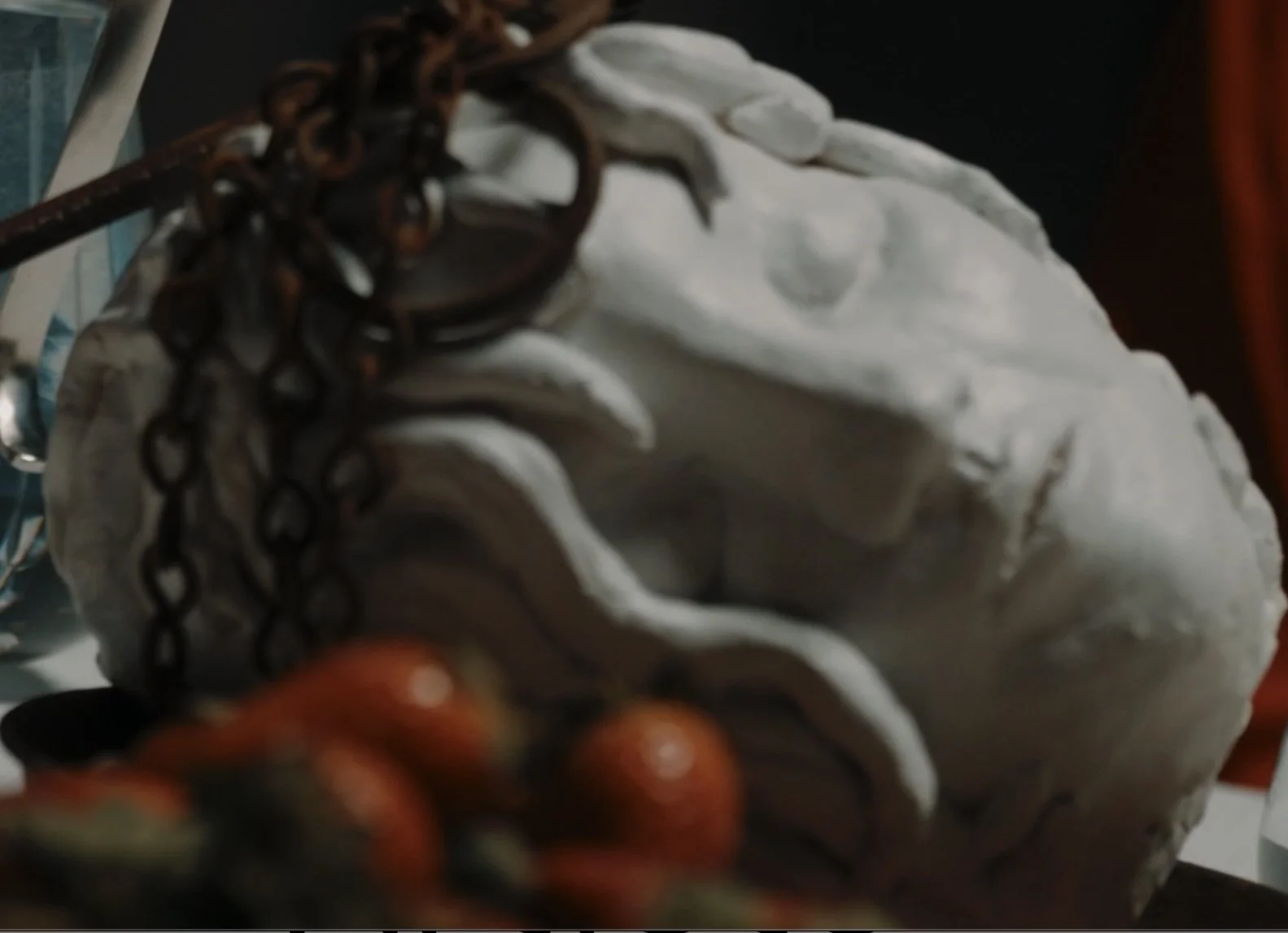 Close-up of a white sculpture or bust of a person's head, with some dark metal chains and an orange object in the foreground.