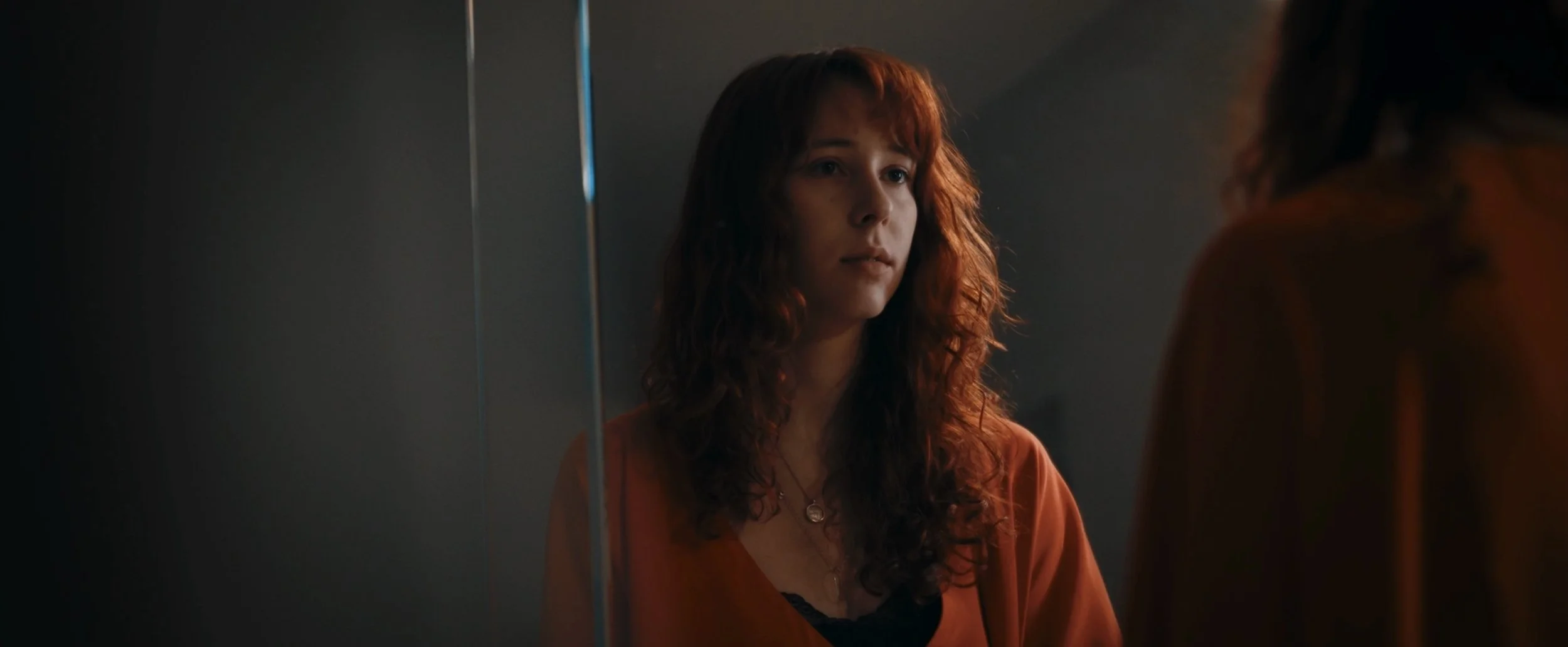 A woman with curly red hair looking at her reflection in a mirror.