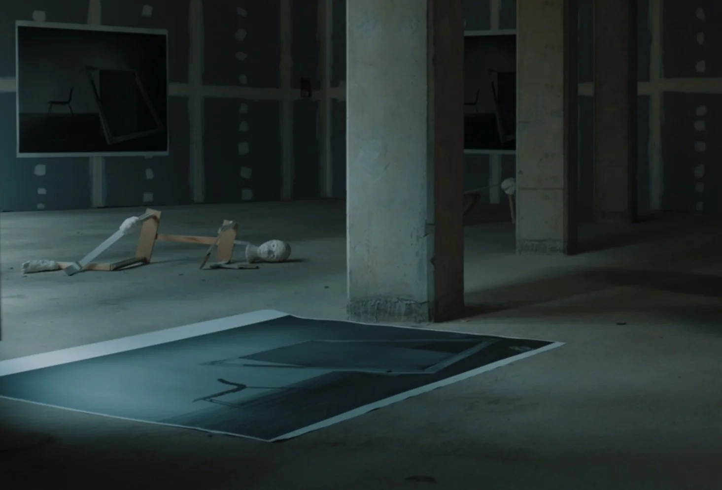An empty building interior under construction with a broken mannequin lying on the floor, construction materials, and a large photo or poster on the floor near a concrete pillar.