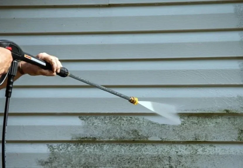 Person using a pressure washer to clean exterior siding of a house.