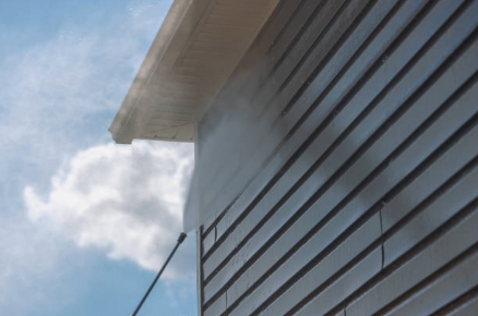 A house with vinyl siding being power washed, with water and steam visible on the side of the house.