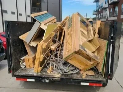 A pickup truck bed filled with discarded wooden furniture and various debris on a city street.