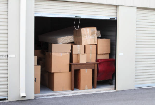 Storage unit with cardboard boxes, a mattress, and a red chair inside.