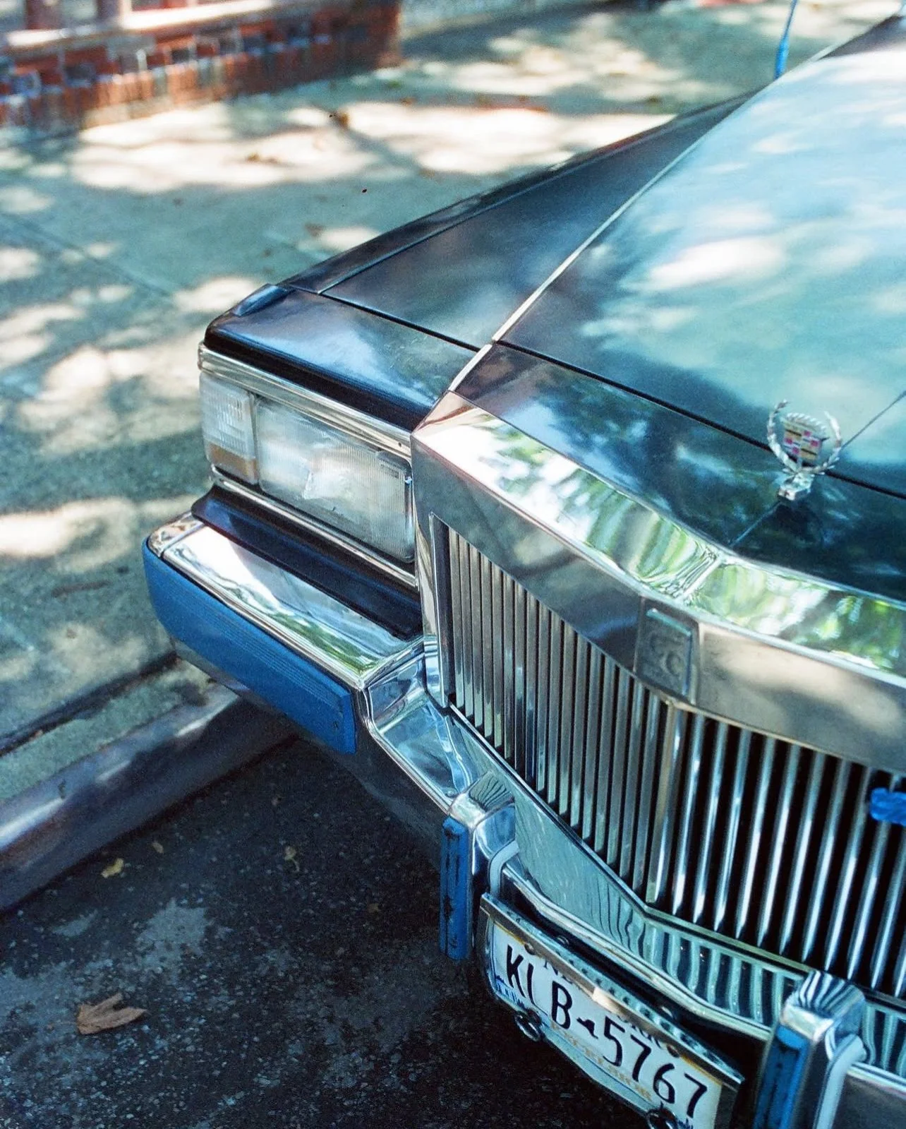 vintage Cadillac with a chrome grille and bumper, blue and silver color, parked on a street.