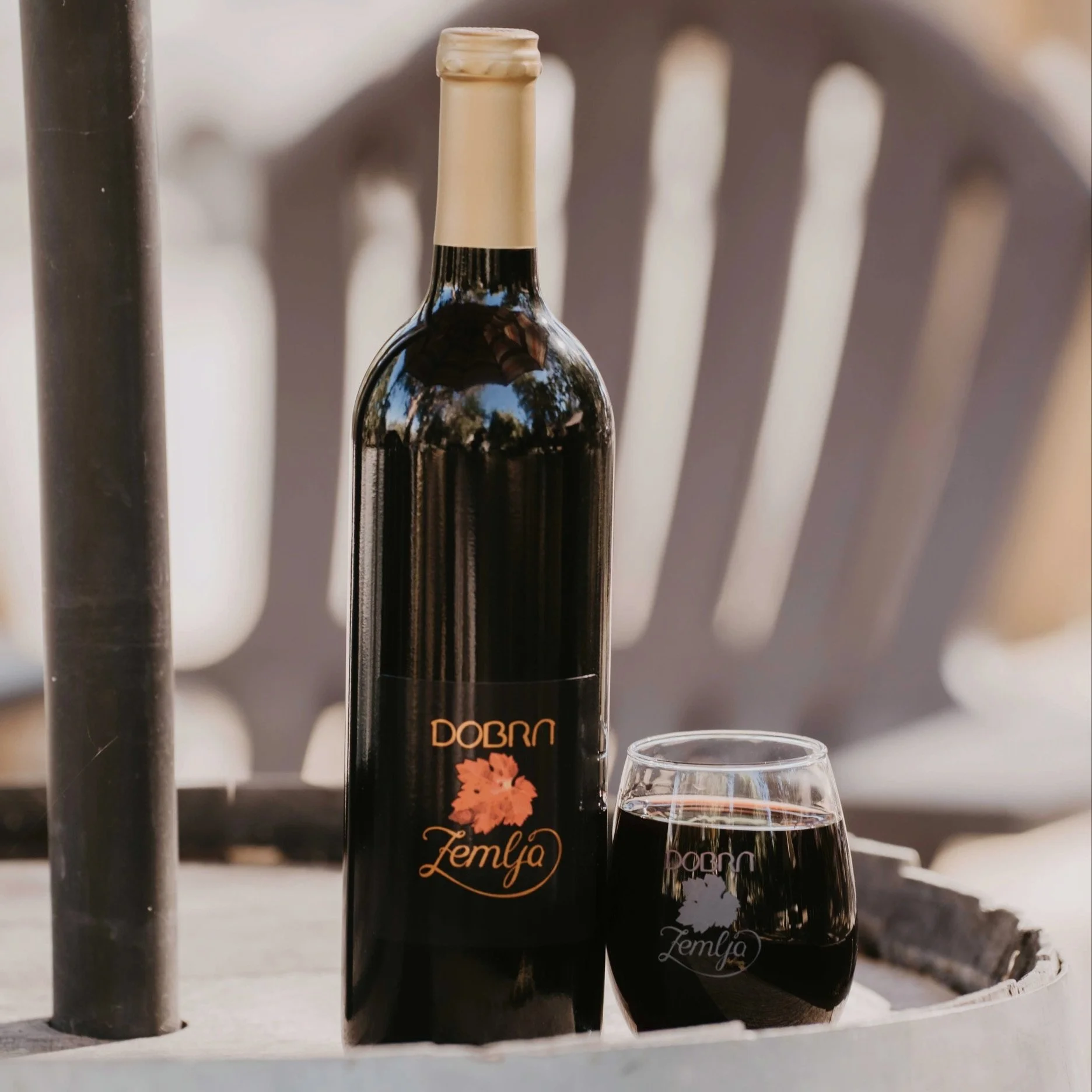 A bottle of red wine labeled 'Dobra Zemlja' and a glass of red wine placed on a wooden barrel table.