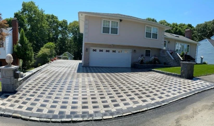 Residential house with a patterned concrete driveway and a well-maintained lawn, trees in the background.
