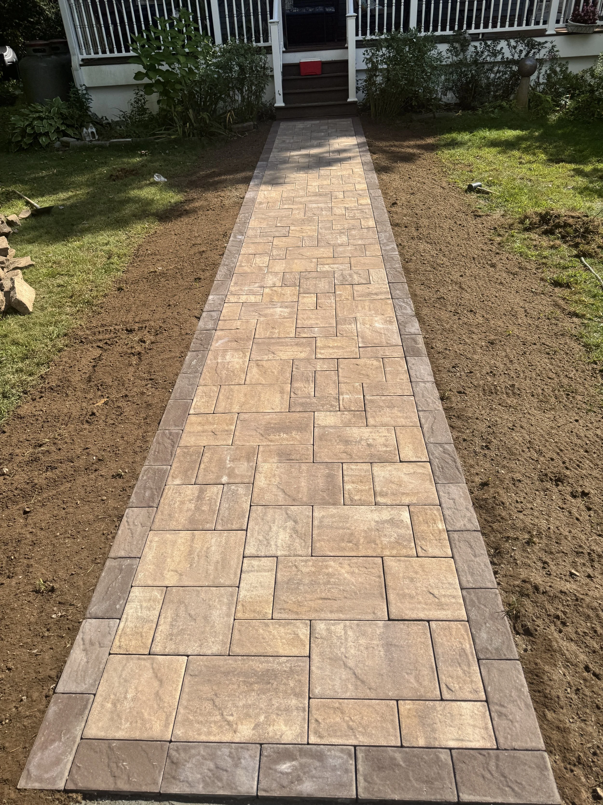 Completed stone pathway leading to porch steps with plants and a garden on either side.