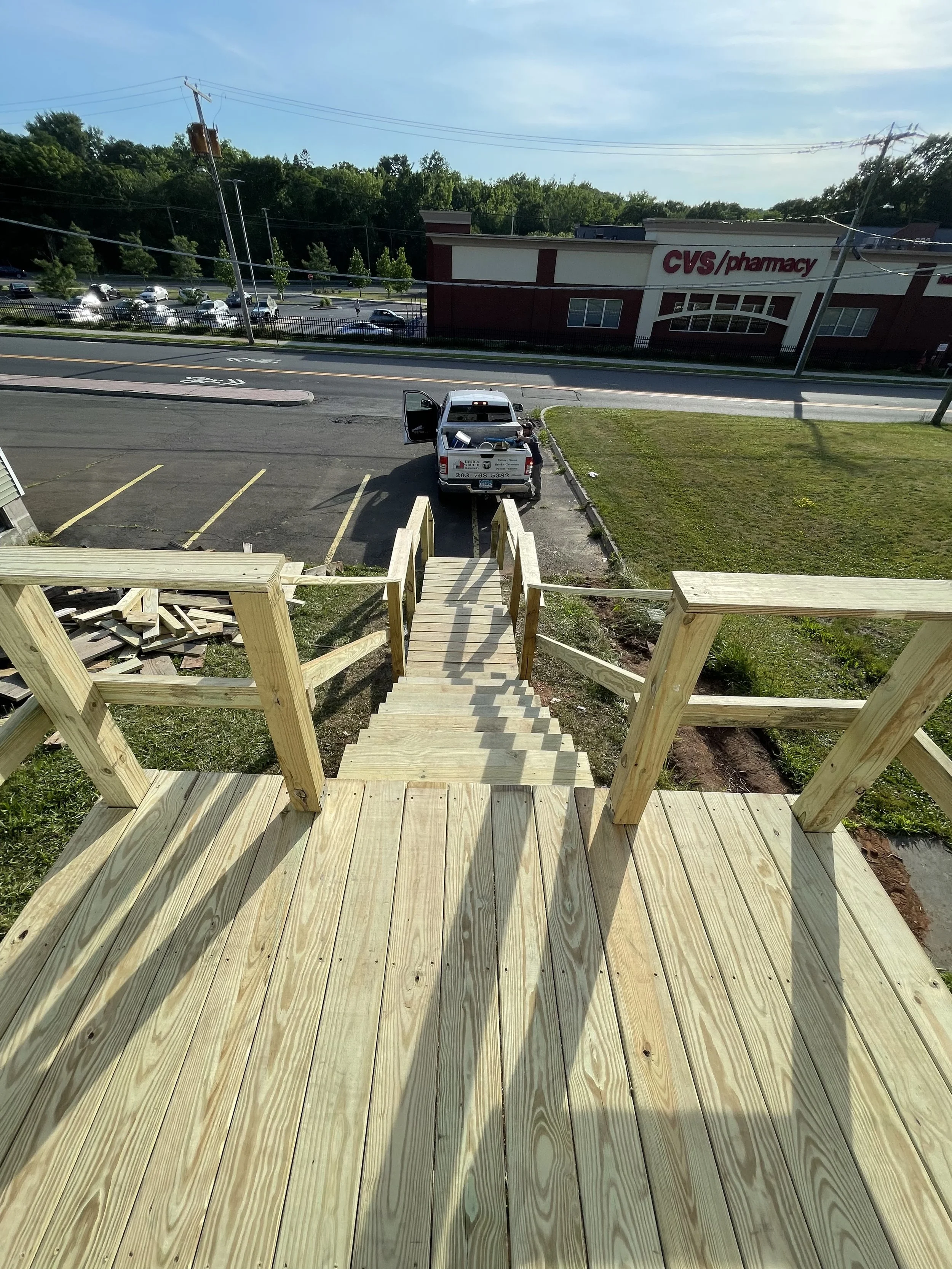 View from a wooden staircase looking down at a parked SUV on the street with a CVS pharmacy in the background.