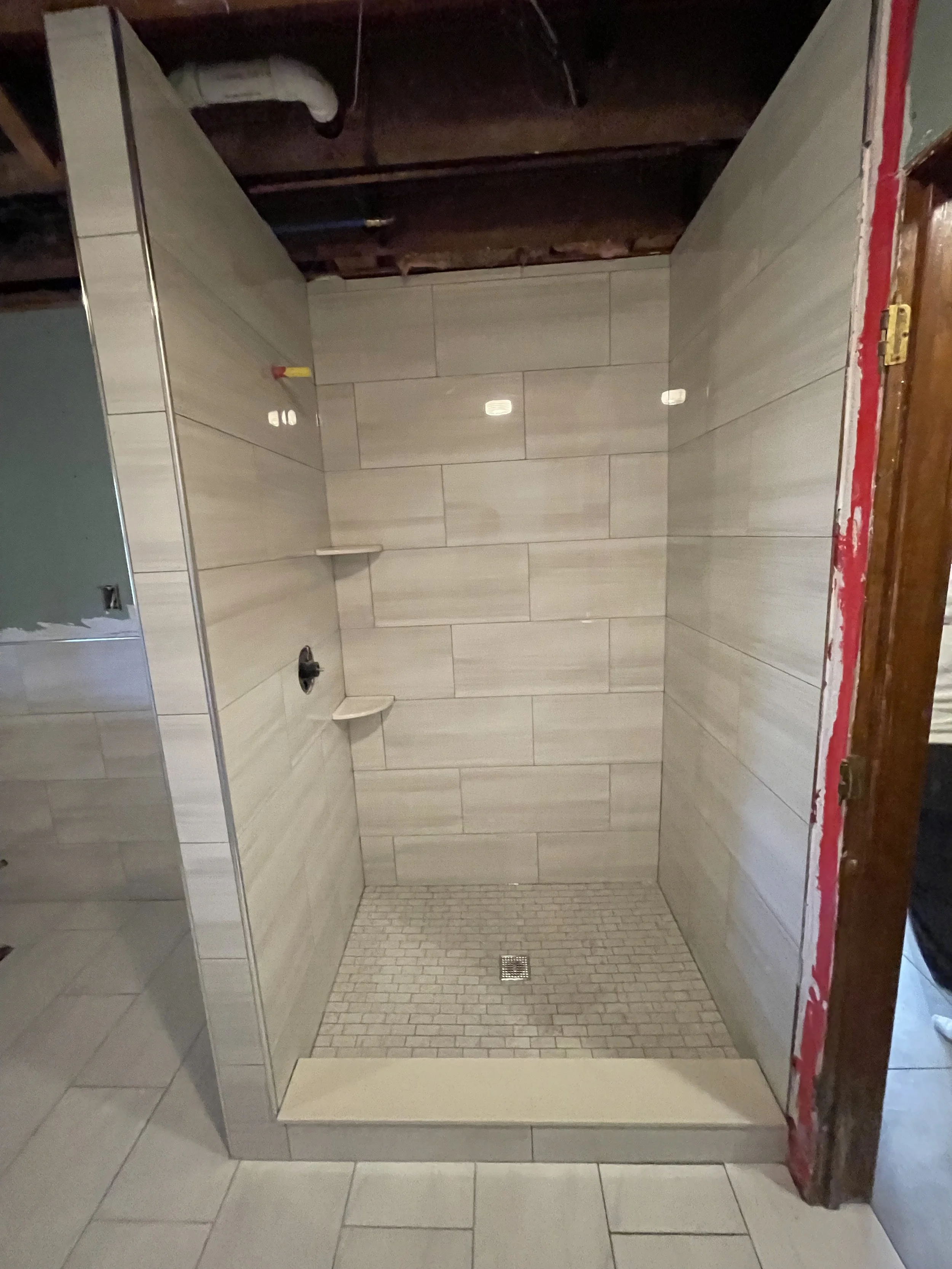 Empty walk-in shower with beige tile walls, a small built-in shelf, and a drain on the tiled floor.
