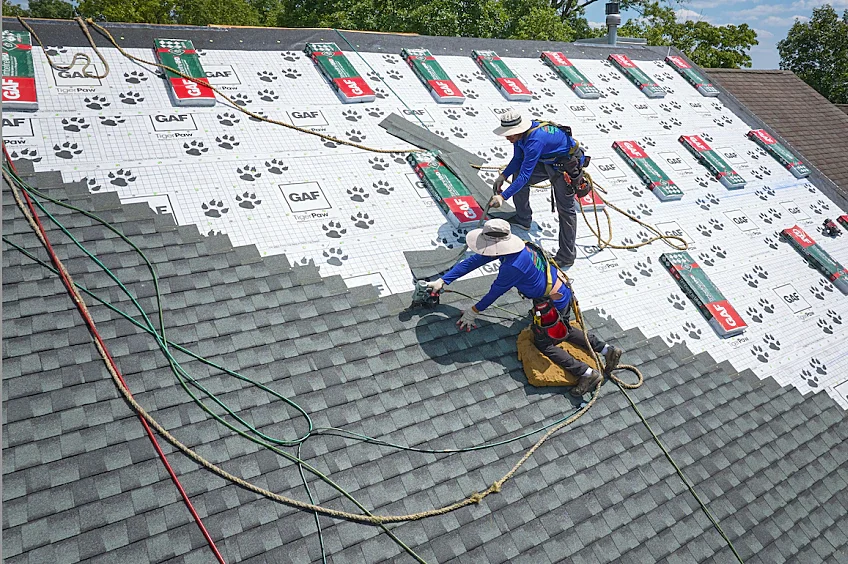 Two workers installing solar panels on a roof, with some roofing shingles visible on the lower section.
