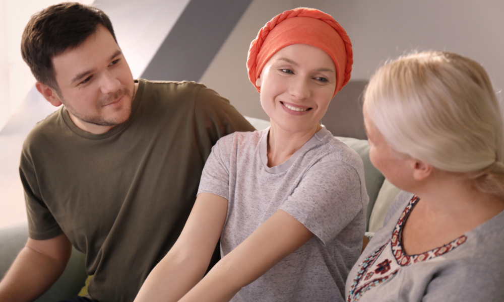 A woman wearing a headscarf and a gray T-shirt sitting with a man and an older woman, smiling and having a conversation in a cozy indoor setting.