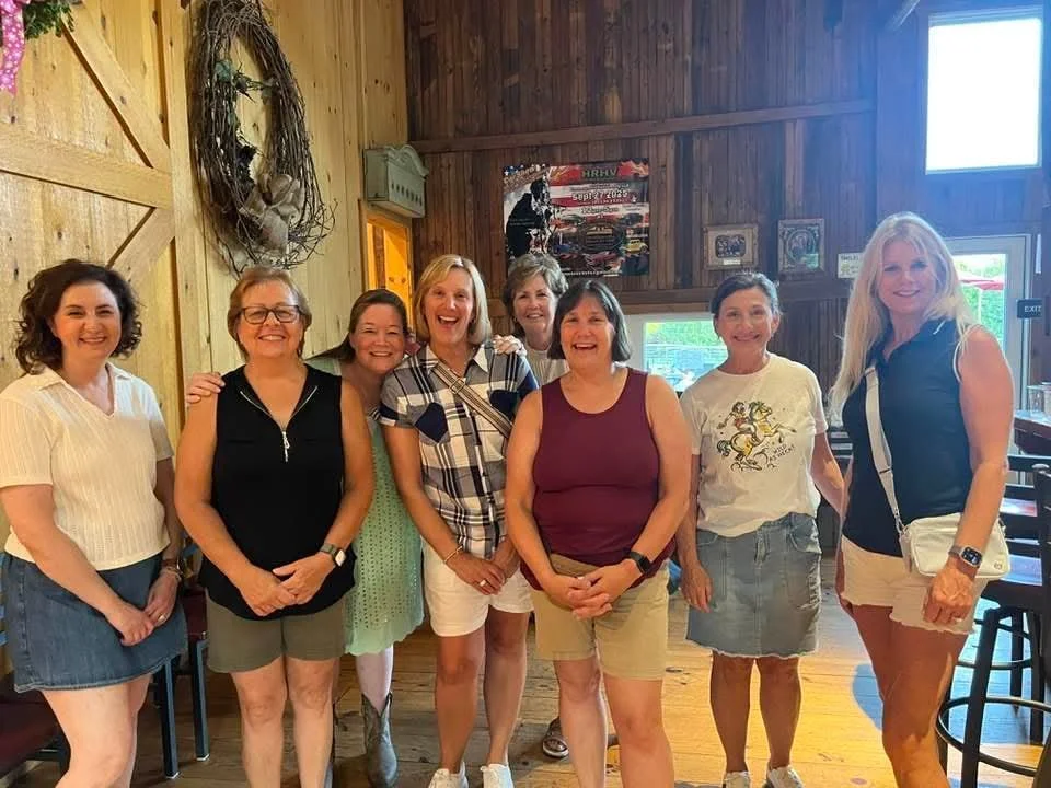 A group of eight women standing inside a rustic wooden building, smiling for the photo.