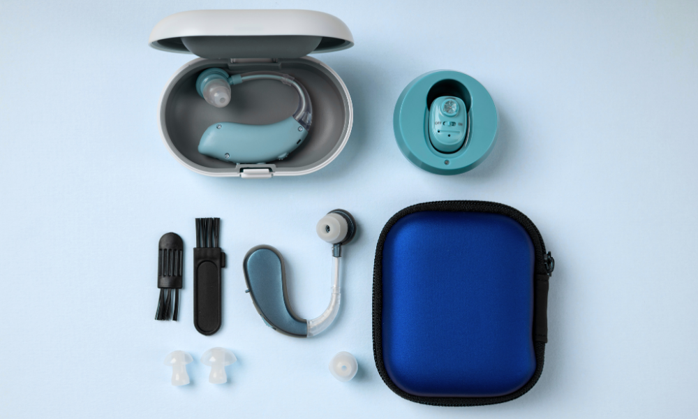 View of a blue and gray hearing aid with accessories, storage case, and cleaning tools arranged on a light blue surface.