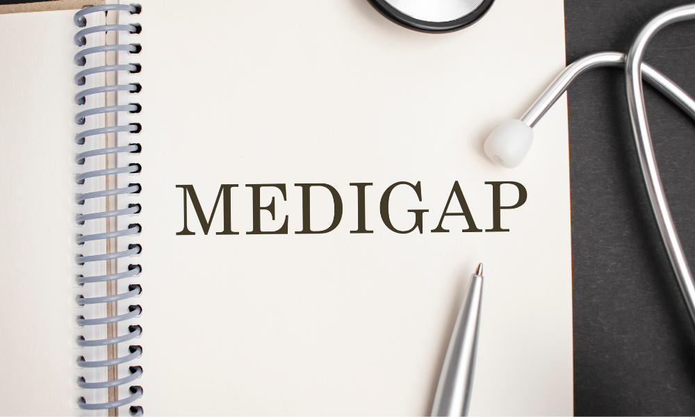 A spiral-bound notebook with the word "MEDIGAP" written on a page, surrounded by a stethoscope, a pen, and a black background.