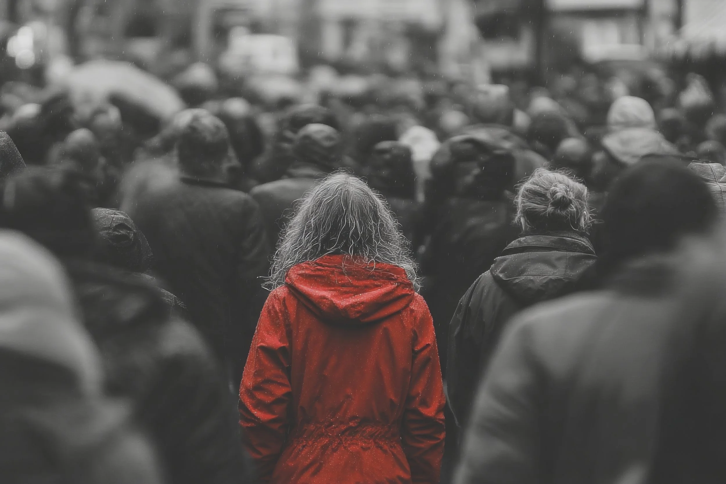 Une foule de personnes vu de dos, avec une femme en manteau rouge au centre, la seule en couleur, le reste de la photo en noir et blanc.