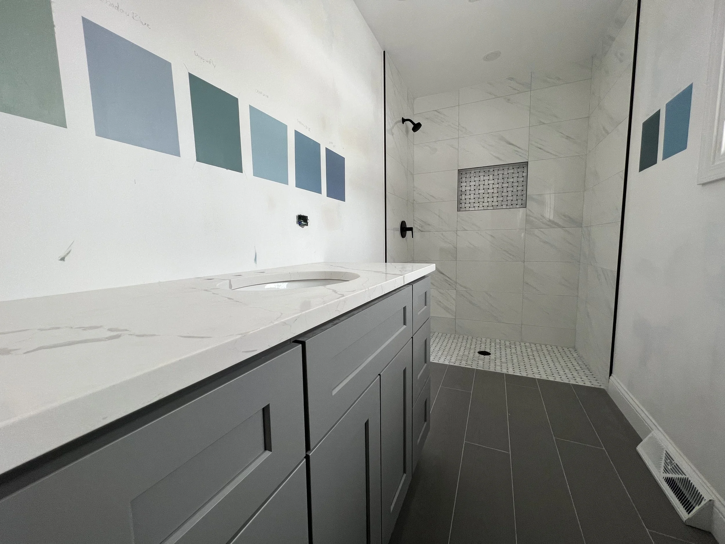 Modern bathroom with gray vanity, white marble countertop, and a walk-in shower with marble tiles and a small niche.