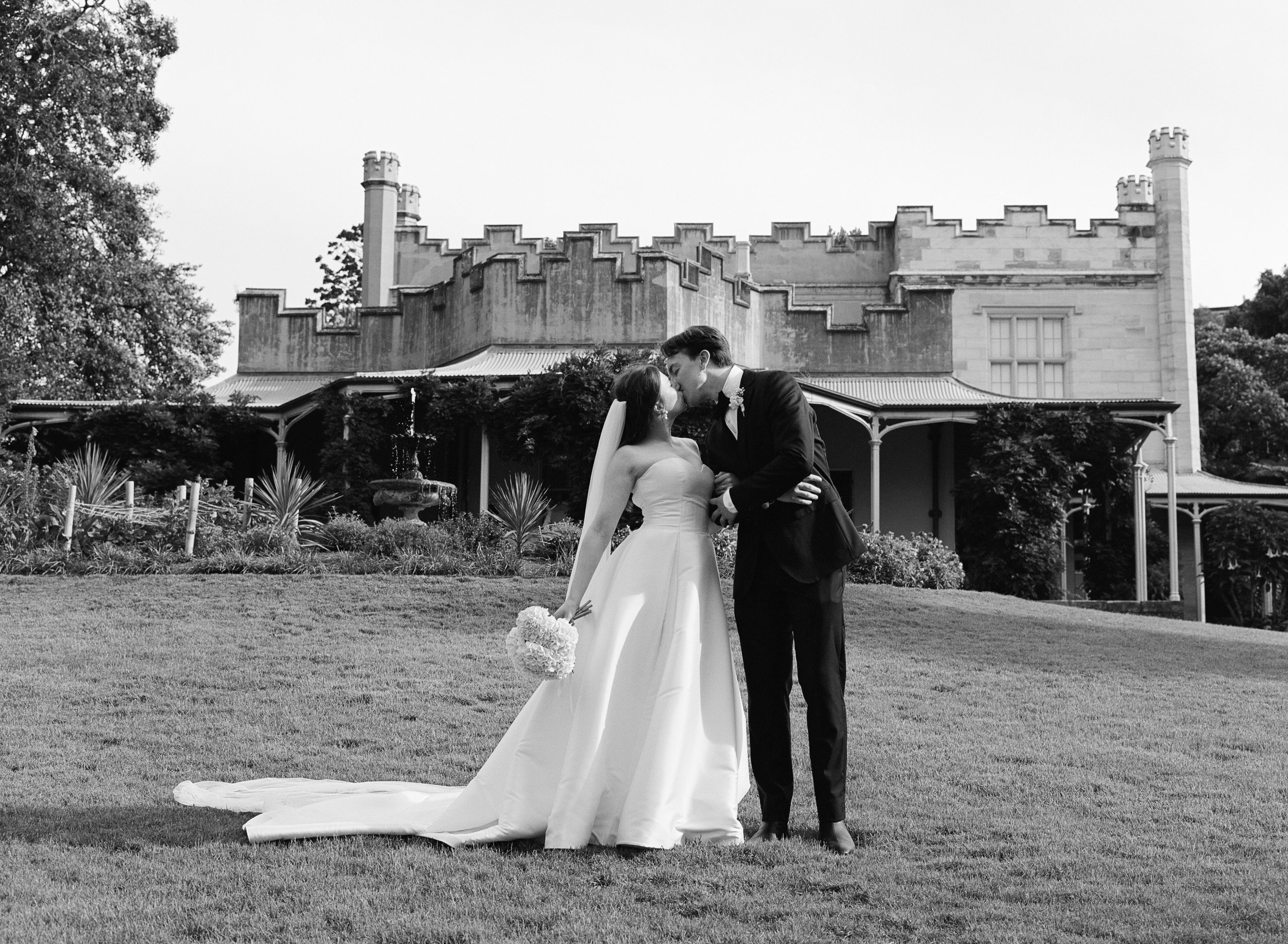 Bride and groom kissing in front of a classic wedding venue, captured in black and white photography