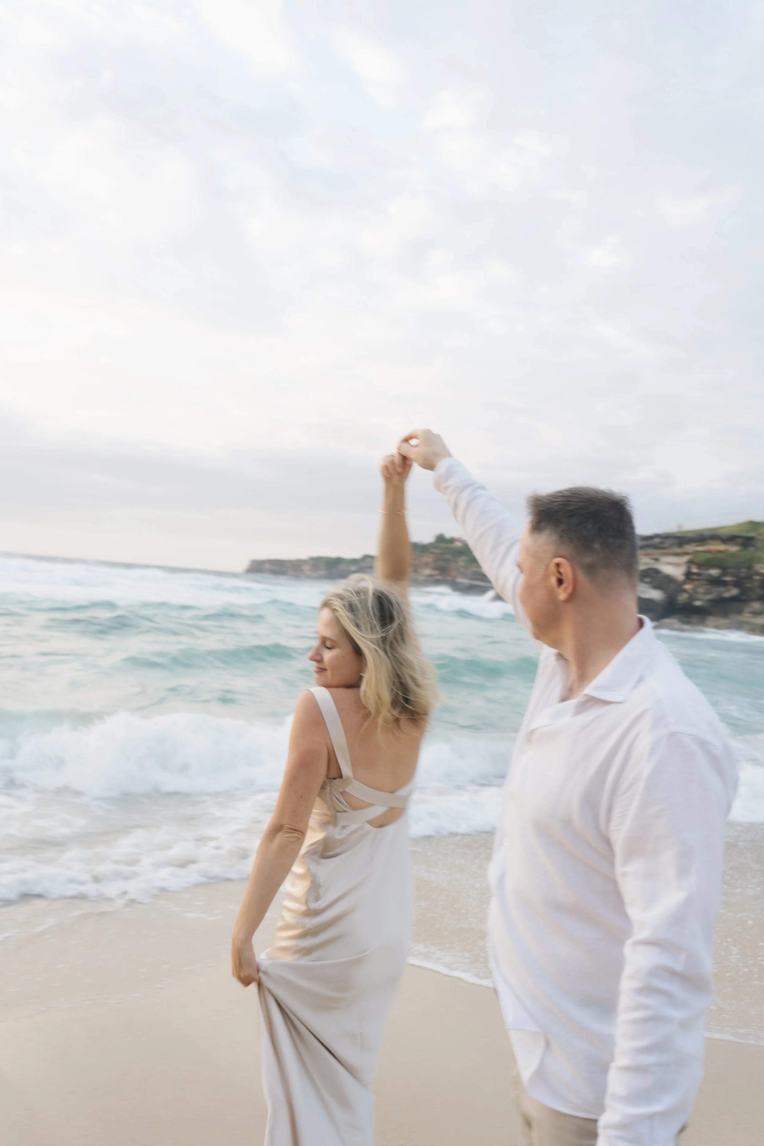 Engaged couple spinning together on the beach, captured in a candid and joyful engagement photography