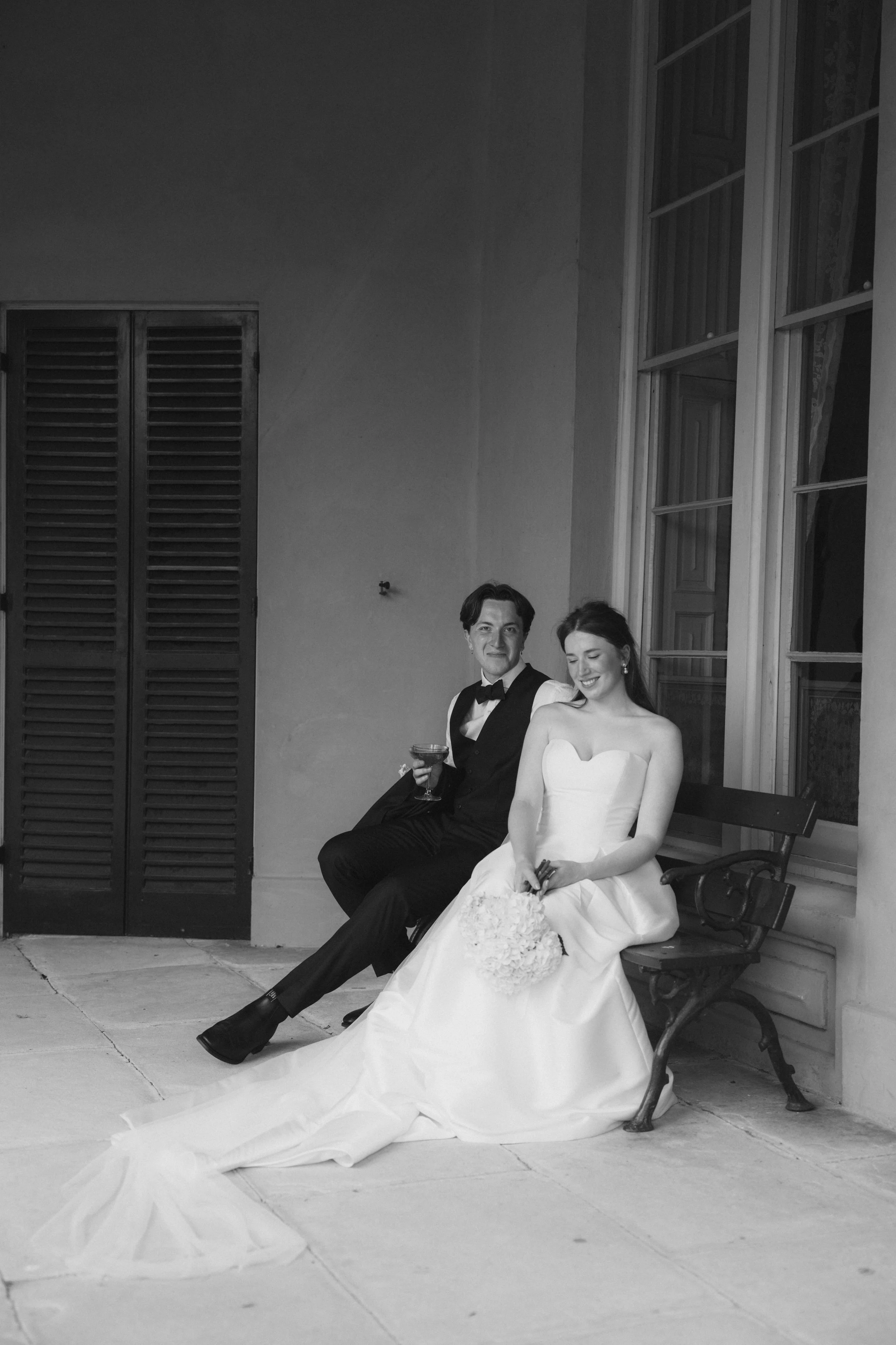 Candid black and white wedding photograph of bride and groom sitting together under a veranda, captured on film