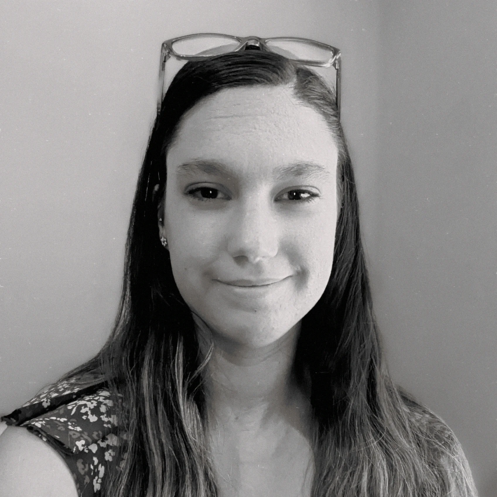 Black and white photo of a woman with long dark hair, wearing glasses on her head and earrings, smiling slightly, against a plain background.