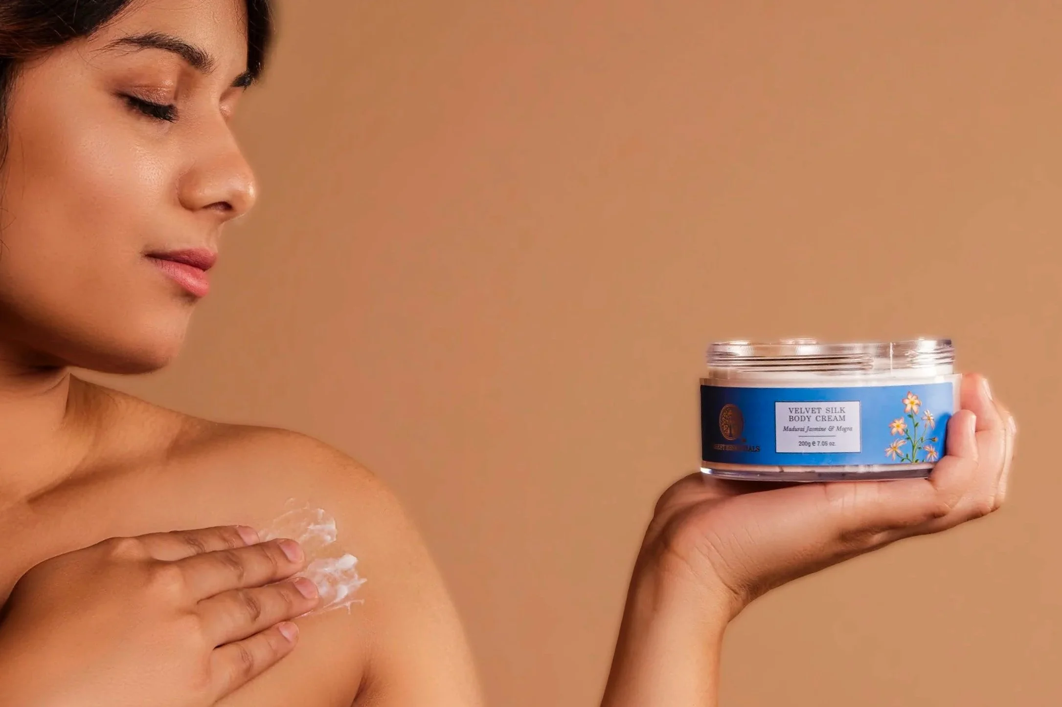 A woman applying body cream to her shoulder, holding a container of Velvet Silk Body Cream, with the label visible.
