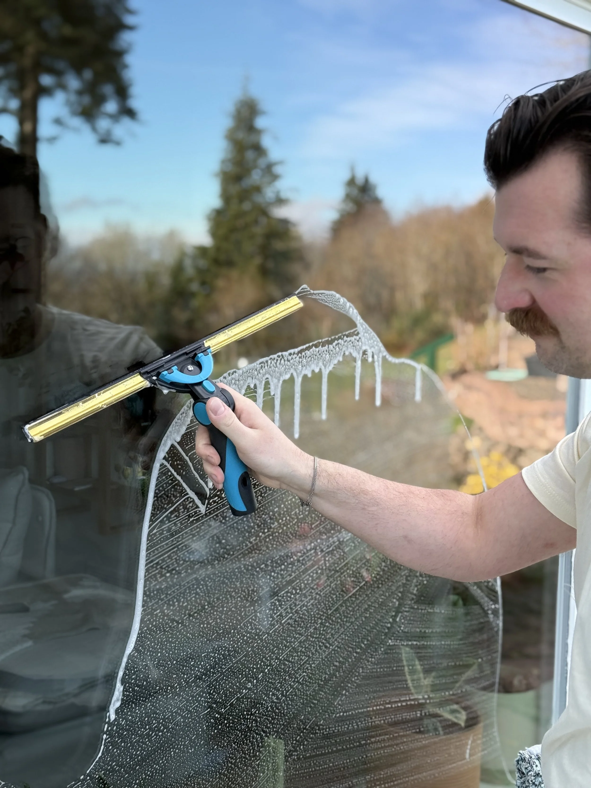 A man cleaning a large glass window with a squeegee and soap, during the daytime outdoors.