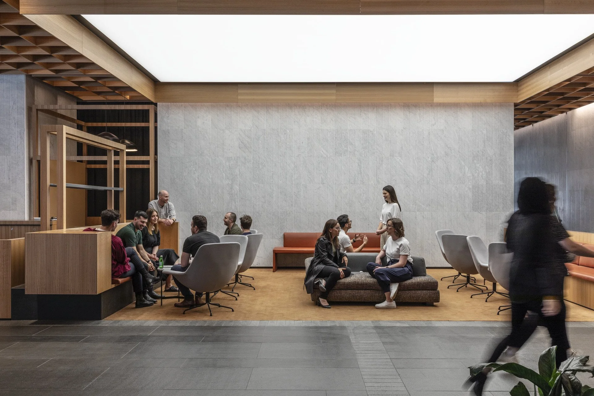 People socializing in a modern lounge area with wooden accents, a high ceiling, and stylish chairs and sofas.