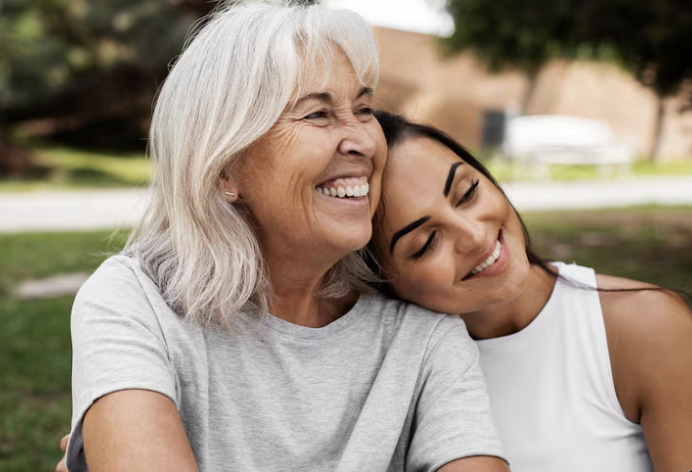 Two women smiling and hugging outdoors in a park.