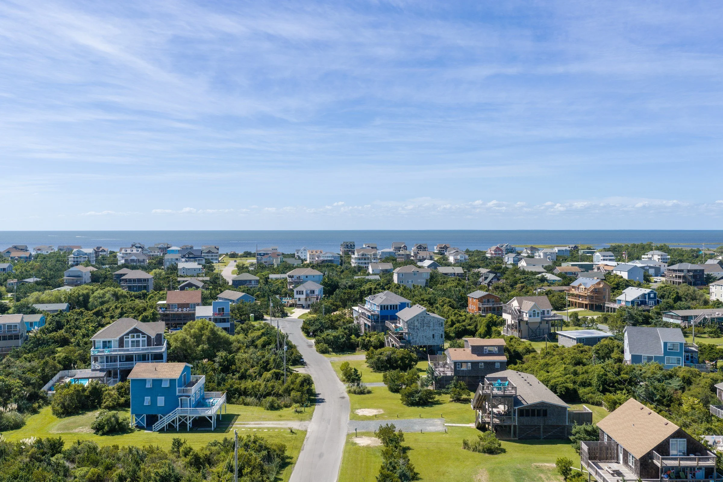 Aerial view along a residential street toward the ocean, showing neighboring homes and vegetation.