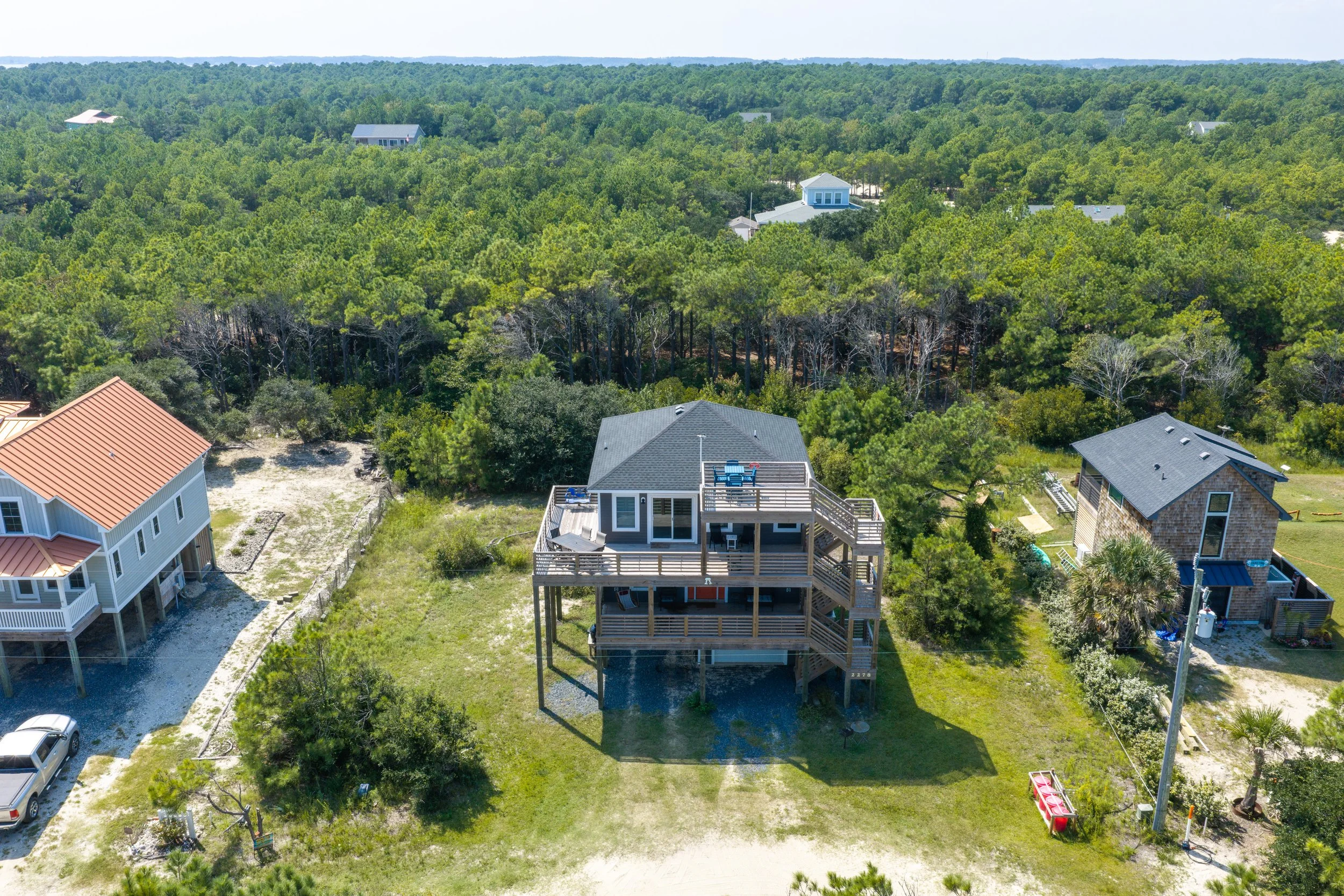 Aerial of an Outer Banks house on a sandy lot backed by pine woods