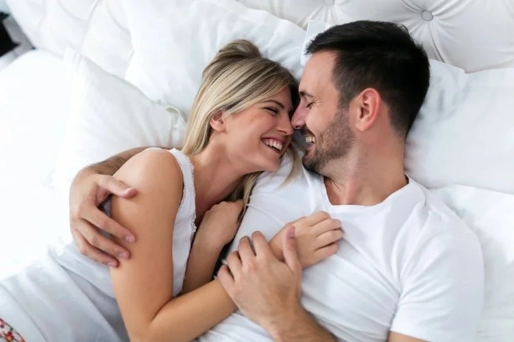 photo of couple smiling in bed together after having pain-free intimacy from working with local pelvic floor therapist for painful sex