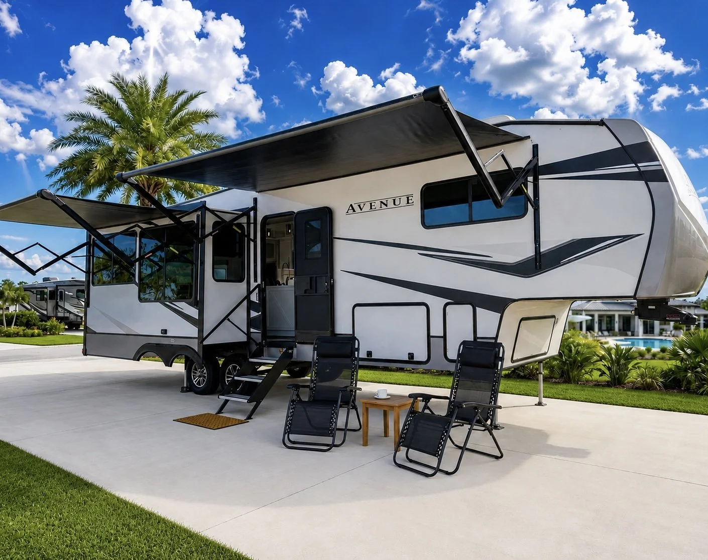 A white RV with black and gray accents parked on grass during sunset, with an outdoor seating area including chairs, a small table, a cooler, and a fire pit.
